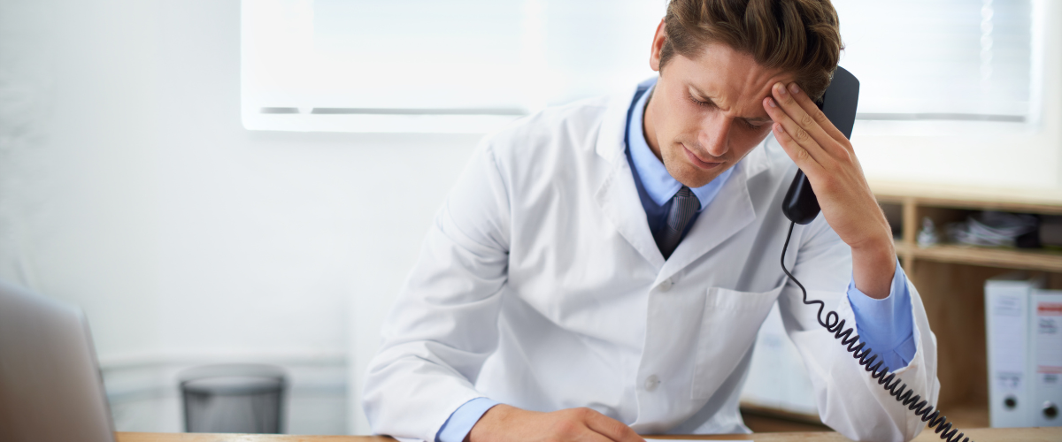 Frustrated doctor is reviewing documents while sitting at his desk