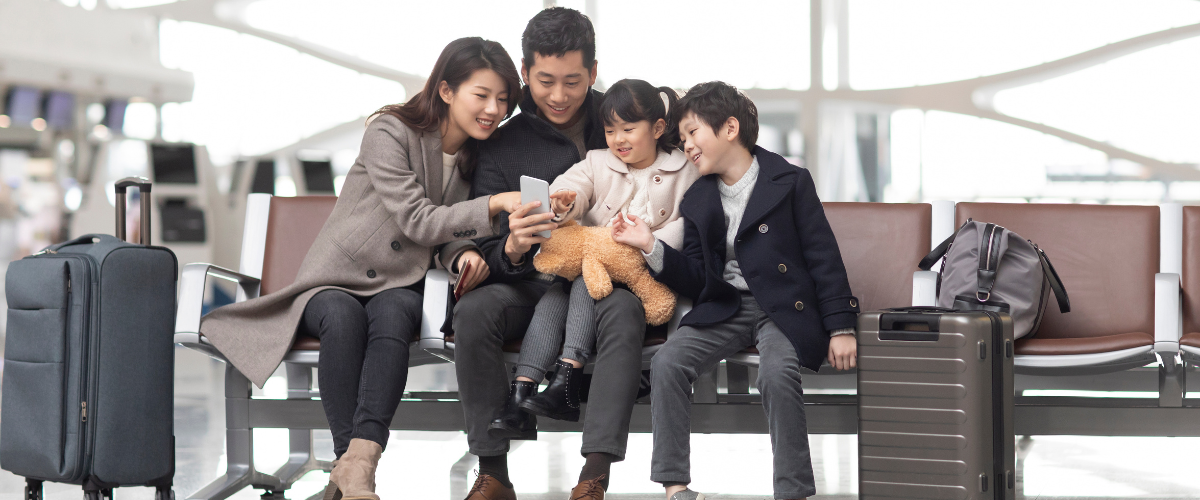 An excited mother, father, son, and daughter sit in an airport.